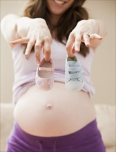 Young pregnant woman showing two different baby shoes. Photo : Mike Kemp