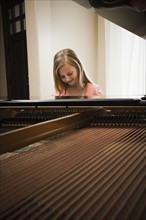 Girl (8-9) playing on grand piano. Photo : Mike Kemp