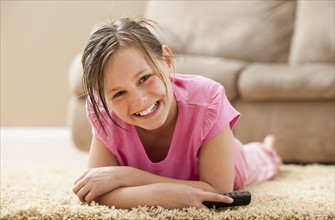 Portrait of girl (10-11) lying on floor holding remote control. Photo : Mike Kemp