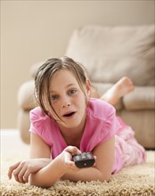 Portrait of girl (10-11) lying on floor holding remote control. Photo: Mike Kemp