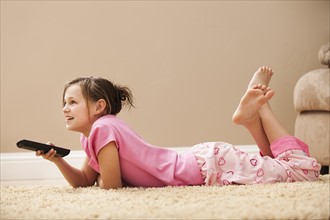 Girl (10-11) lying on floor holding remote control. Photo: Mike Kemp