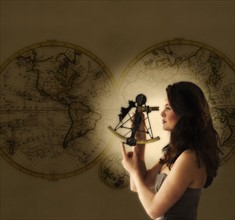 Woman looking through antique sextant, world map in background.