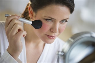 Woman applying blush on cheekbones.