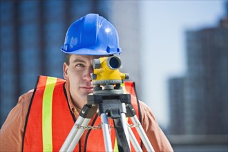 USA, New Jersey, Jersey City, construction worker in hard hat using theodolite.