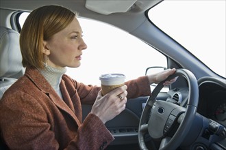 Woman driving car and drinking coffee.