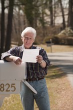 USA, Virginia, Richmond, senior man reading letters by mailbox. Photo: Mark Edward Atkinson