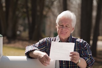 USA, Virginia, Richmond, senior man reading letter by mailbox. Photo: Mark Edward Atkinson