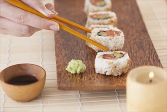 Woman holding sushi by chopsticks.