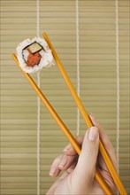 Woman holding sushi by chopsticks.