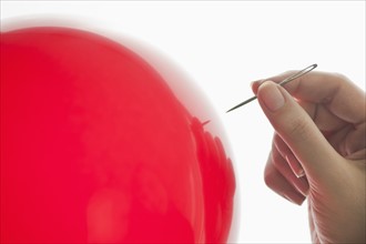 Studio shot of woman holding needle close to red balloon.