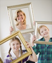 Mother and daughters (8-11) holding picture frames. Photo : Jamie Grill Photography