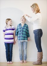 Mother measuring daughters' (8-11) height. Photo : Jamie Grill Photography