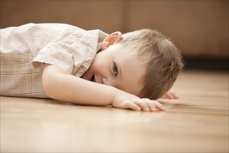 Portrait of smiling boy (2-3) lying on floor. Photo: Mike Kemp