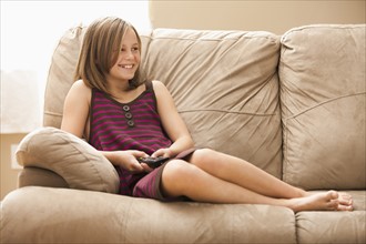 Girl (10-11) sitting on sofa, watching TV. Photo: Mike Kemp