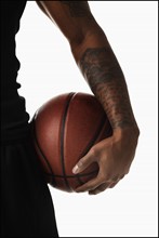 Midsection of tattooed man hooding basketball. Photo : Mike Kemp