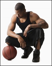 Studio shot of man with basketball crouching. Photo : Mike Kemp