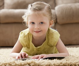 Portrait of smiling girl (2-3) lying on rug with book. Photo : Mike Kemp