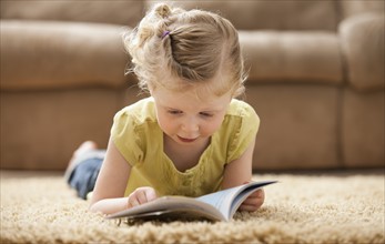 Girl (2-3) lying on rug, reading book. Photo : Mike Kemp