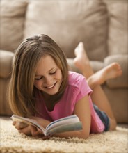 Girl (10-11) lying on rug, reading book. Photo : Mike Kemp