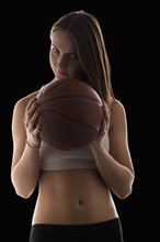 Studio portrait of young woman holding basketball. Photo : Mike Kemp