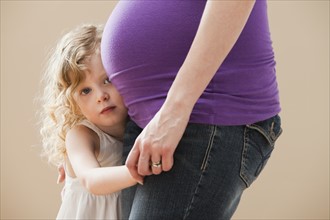 Girl (2-3) peeking form behind pregnant mother's belly. Photo : Mike Kemp