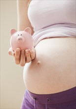 Young pregnant woman holding pink piggybank. Photo: Mike Kemp