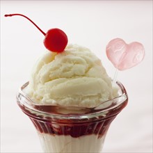 Close up of ice cream dessert with cherry on top and heart shaped decoration.