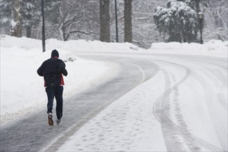 USA, New York City, man jogging up snowy road. Photo: fotog
