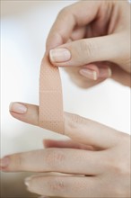 Studio shot of woman sticking adhesive bandage on finger.
