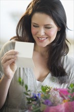 Young woman holding bouquet and reading greeting card.