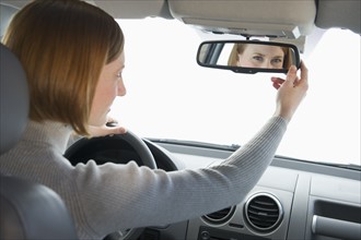 Woman driving car and adjusting mirror.