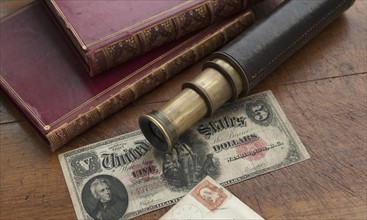 Close up of antique telescope, books and banknote.