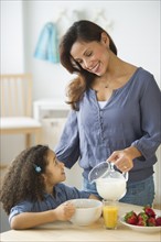 Mother pouring milk for daughter (6-7) during breakfast.