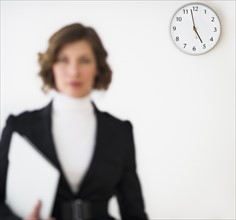 Defocused businesswoman with office clock showing time in background.