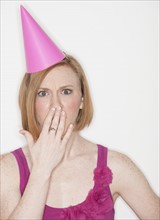 Woman wearing pink party hat covering lips with hand.