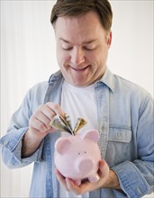 Man putting money into piggy bank. Photo: Jamie Grill Photography
