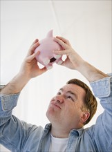 Man shaking piggy bank. Photo : Jamie Grill Photography