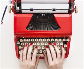 Close up of woman's hands with red nail polish typing on antique typewriter.