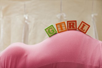 Wooden blocks with letters on pregnant woman's belly, reading as girl. Photo : Mike Kemp