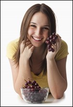 Studio portrait of young woman holding grapes. Photo : Mike Kemp