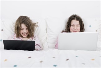 Girls (6-7,8-9) with laptops sitting in bed. Photo : Justin Paget