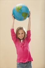 Studio portrait of girl (8-9) holding globe. Photo: Mike Kemp
