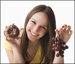 Studio portrait of young woman holding grapes and doughnut. Photo : Mike Kemp
