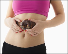 Young woman holding doughnut against belly. Photo : Mike Kemp