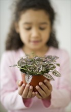 Portrait of defocused girl (6-7) holding potted plant.