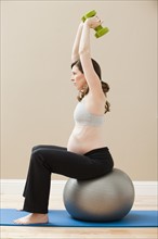 Young pregnant woman exercising with dumbbells and fitness ball. Photo : Mike Kemp