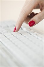 Close up of woman's finger with red nail polish typing on computer keyboard.