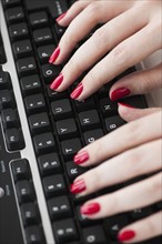 Close up of woman's fingers with red nail polish typing on computer keyboard.