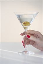 Close up of woman's hand with nail polish holding martini glass with olive.