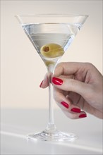 Close up of woman's hand with nail polish holding martini glass with olive.